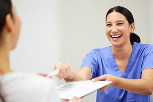 a front desk staff member handing a patient forms to fill out