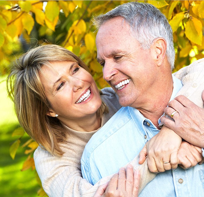 Smiling older woman holding smiling older man from behind outdoors