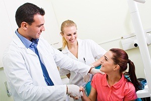 Dentist shaking hands with woman in dental chair