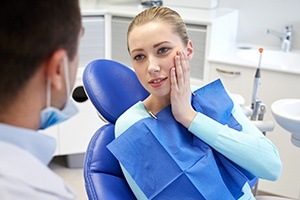 Woman in dental chair holding cheek