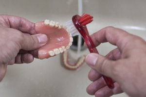 a person brushing their dentures in a sink