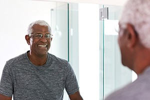 Older man with dental implants in Dallas smiling in mirror