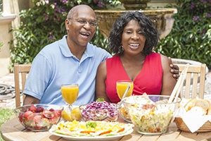 man and woman sitting at a table filled with various foods 