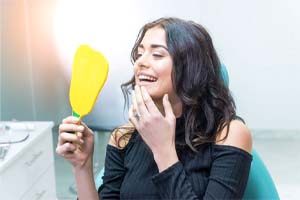 woman admiring her smile in a mirror after getting veneers 