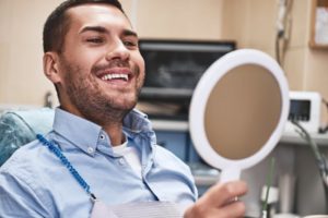 patient looking in the mirror after being treated by their emergency dentist in Dallas