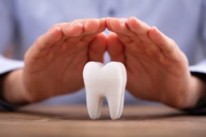 a person holding their hands over a model of a tooth to signify that they're protecting the enamel