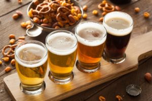 a flight of craft beers with a bowl of bar snack mix next to it