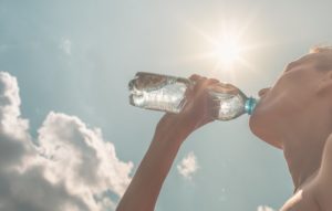 a person drinking water beneath the summer sun