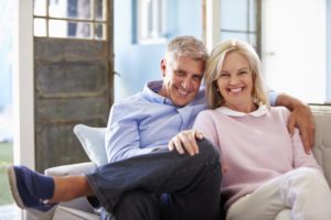 smiling senior man and woman with implant dentures sitting on their couch 
