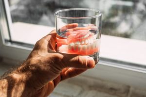 a person holding a glass of room temperature water with dentures in it