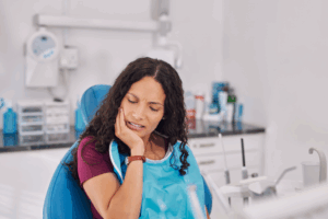 a woman sitting in a dental chair holding her mouth in pain